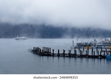 Scenery of beautiful Lake Chuzenji 中禅寺湖 on a foggy autumn day, with wooden piers extending from the lakside and sightseeing boats cruising on the misty water, in Nikko National Park, Tochigi, Japan - Powered by Shutterstock