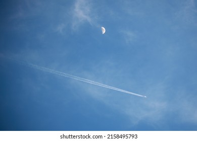A scenery of blue sky with chemtrails and the Moon in first quarter