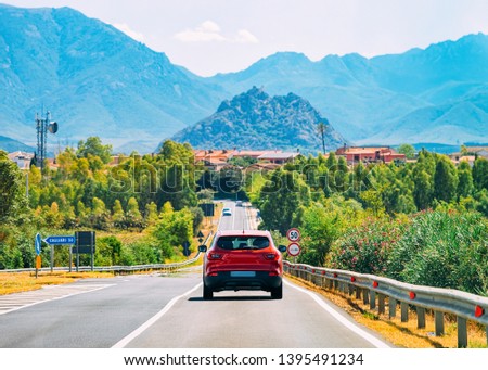 Scenery with red car on the highway in Carbonia near Cagliari in Sardinia in Italy. Nature and Automobile back in the road. Mountains and hills on the background