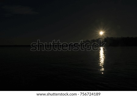 scenery at the river estuary by using high apature openings. there is a reflection of the sun on the water. there is a silhouette effect on the lines and trees.