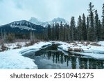 Scenery of rocky mountains and pine forest on frozen lake in gloomy at Canmore, Canada