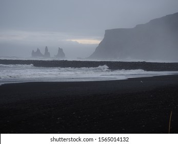 A scenery of a South Iceland beach (Vík í Mýrdal), black sand beach, huge rocks (Reynisdrangar), unusual coastal scenery, Iceland South coast, basalt, rough sea, pale milky dim natural light, winter  - Powered by Shutterstock