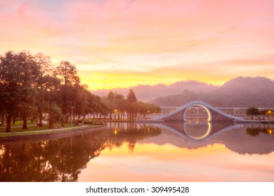 Scenery of an urban park lit up by golden sunlight with reflections of an arch bridge and glowing sky on the smooth lake water ~ Early morning scene of Dahu Community Park in Neihu,Taipei City Taiwan - Powered by Shutterstock