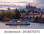 Scenery of Vltava River at sunset with the majestic Prague Castle and St. Vitus Cathedral under twilight sky in background and tourist boats cruising under Charles Bridge, in Old Town Prague, Czech