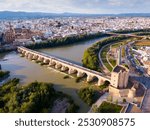 Scenic aerial view of ancient Roman bridge across Guadalquivir river and Moorish architecture of Mezquita-Catedral on background with Cordoba cityscape, Spain