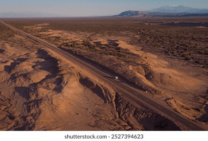 A scenic aerial view of a deserted road through the arid, rocky landscape of Talampaya National Park in Argentina, with distant mountains under the warm light of either sunrise or sunset. - Powered by Shutterstock