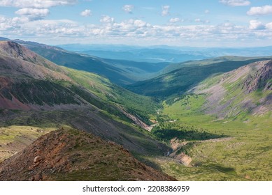 Scenic aerial view from mountain pass to green forest valley among mountain ranges and hills on horizon at changeable weather. Green landscape with sunlit mountains under cumulus clouds in blue sky. - Shutterstock ID 2208386959