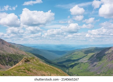 Scenic aerial view from mountain ridge to green forest valley among mountain ranges and hills on horizon at changeable weather. Green landscape with sunlit mountains under cumulus clouds in blue sky.
