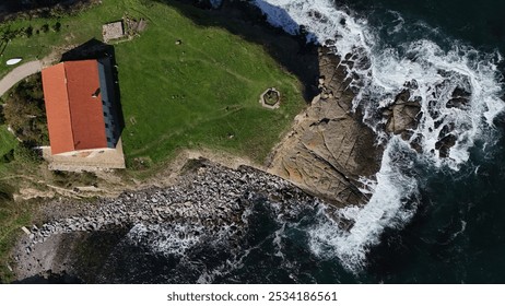 A scenic aerial view of a rugged coastline featuring a solitary house on a cliff, surrounded by crashing waves. The coastal town in the distance adds charm to the natural beauty of the rocky shore and - Powered by Shutterstock