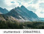 Scenic alpine landscape with great dragon shaped mountain under cloudy sky. Beautiful mountain scenery with big sharp rocks in cloudy sky above coniferous forest. Awesome high mountain with peaked top