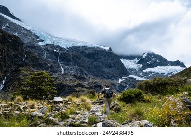 A scenic alpine meadow with wildflowers, featuring multiple waterfalls cascading down rocky cliffs with snow-capped mountains in the background. - Powered by Shutterstock