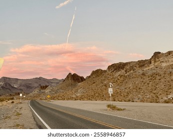 Scenic Arizona desert road at dusk, surrounded by rugged mountains and soft pink clouds in the sky. A peaceful, open landscape with a glowing sunset and a lone contrail streaking above. - Powered by Shutterstock