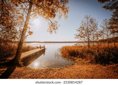 Scenic autumn lakeside view with a wooden dock, calm water, and golden foliage under a bright sun, creating a serene and peaceful atmosphere. - Powered by Shutterstock