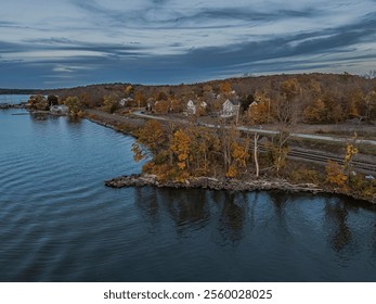 Scenic autumn view of a lakeside village with colorful foliage and calm water, under a dramatic sky. - Powered by Shutterstock