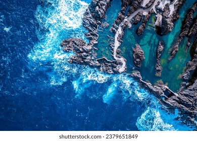 Scenic, beautiful bird's eye view of people swimming in the natural lava pools in Porto Moniz, Madeira, Portugal, while the sea rages around them - Powered by Shutterstock