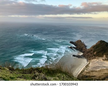 Scenic Birds Eye View From A Hilltop To A Beach Surrounded By Rocks And Whitecaps In The Ocean Near Cape Reinga, New Zealand