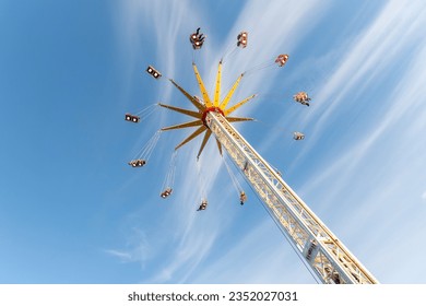 Scenic bottom view high chain swing flying carousel against blue sky. Merry go round roundabout chairoplane at portable amusement park. People enjoy having family fun play riding at fair festival - Powered by Shutterstock