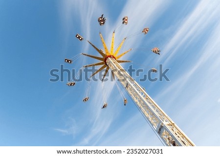 Scenic bottom view high chain swing flying carousel against blue sky. Merry go round roundabout chairoplane at portable amusement park. People enjoy having family fun play riding at fair festival