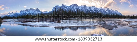 Scenic Bow River Panoramic Landscape with Snowy Mountain Peaks of Rundle Range and Dramatic Sunset Sky above City of Canmore on a cold October Day in Canadian Rocky Mountains