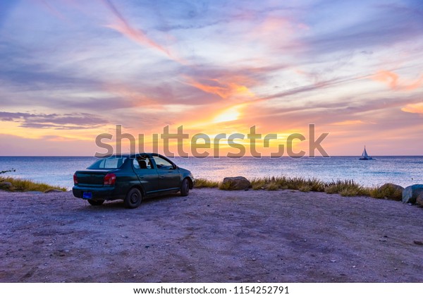 Scenic caribbean sunset with a car near a cliff\
and a boat at the\
horizon