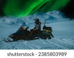Scenic close up side photo of girl sitting on snow mobile with night mountains and northern green lights in starry sky. Driver wear snowmobile helmet and warm overall. Norway, Sweden destinations