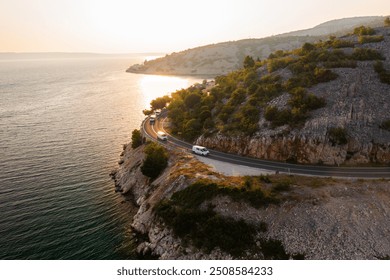 Scenic coastal drive along rocky shoreline at sunset with vehicles on winding road.  - Powered by Shutterstock