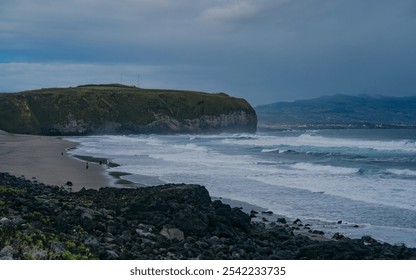 Scenic coastal landscape with dramatic cliffs, a winding coastal road, and waves crashing against the rocky shore under a clear blue sky. The vibrant greenery in the foreground contrasts - Powered by Shutterstock