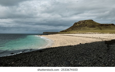 Scenic coastal landscape with a rocky beach, clear turquoise water, and a grassy hill under a cloudy sky in Isle of Skye, Scottish highlands - Powered by Shutterstock