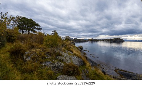 A scenic coastal landscape with rocky shoreline, calm water, and overcast sky. - Powered by Shutterstock