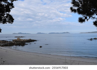 A scenic coastal landscape with a rocky shoreline, calm ocean waters, and distant mountains visible under a partly cloudy sky - Powered by Shutterstock