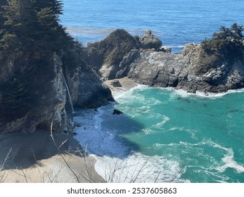 A scenic coastal landscape with turquoise waves, a small waterfall, rocky cliffs, and a secluded beach surrounded by lush greenery. - Powered by Shutterstock