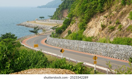 A scenic coastal road in Chanthaburi, Thailand, winds along the lush green hills and rocky shoreline, offering beautiful views of the ocean. The winding curves and surrounding create a peaceful drive. - Powered by Shutterstock