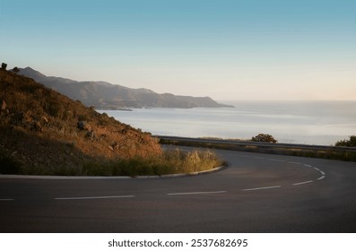 Scenic coastal road with a sharp curve, overlooking a serene sea and mountains in the distance during sunset, creating a calm and peaceful ambiance. - Powered by Shutterstock