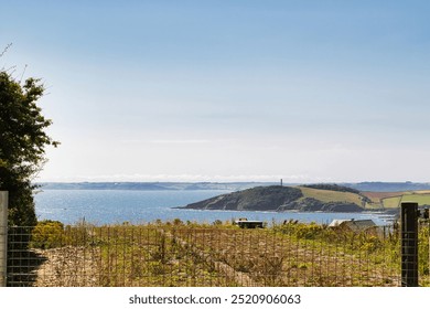 A scenic coastal view featuring a calm sea, distant hills, and a lighthouse on a small island. Cornwall, UK - Powered by Shutterstock