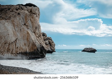 A scenic coastal view featuring a large rocky cliff and a calm sea under a partly cloudy sky. - Powered by Shutterstock