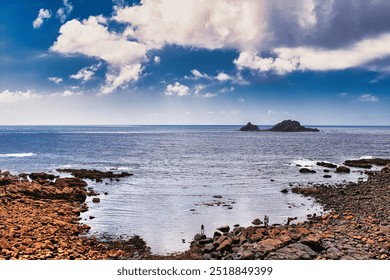 A scenic coastal view featuring rocky shores, calm blue waters, and a distant island under a partly cloudy sky.At Cape Cornwall, UK. - Powered by Shutterstock