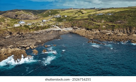 A scenic coastal view featuring rocky shores, clear blue waters, and green hills in the background. At Cape Cornwall, UK. - Powered by Shutterstock