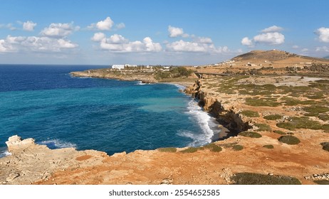 A scenic coastal view featuring rocky cliffs, a vibrant blue sea, and a clear sky with scattered clouds, surrounded by a dry and rugged landscape - Powered by Shutterstock