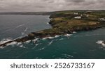 A scenic coastal view featuring rugged cliffs, rolling green hills, and white houses along the shoreline. In Cornwall, UK.