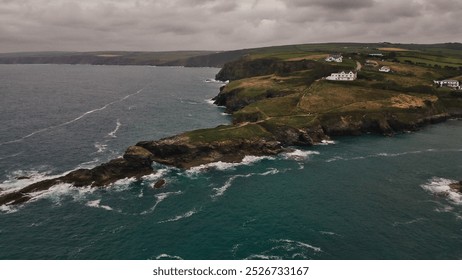 A scenic coastal view featuring rugged cliffs, rolling green hills, and white houses along the shoreline. In Cornwall, UK. - Powered by Shutterstock