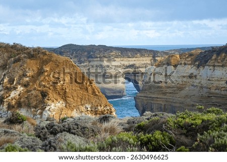 Scenic coastal view at Loch Ard Gorge along Australia's Great Ocean Road. Dramatic limestone cliffs and turquoise waters frame this iconic natural arch under a soft, cloud-filled sky.