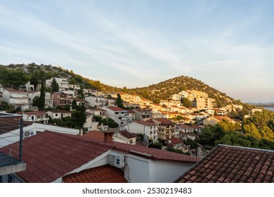 Scenic coastal village at sunset with red-roofed houses, green hills, and tranquil sea view in a peaceful Mediterranean landscape. Concept of summer travel, Mediterranean architecture, and nature.  - Powered by Shutterstock