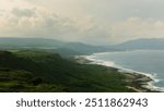 A scenic coastline in Kenting, Taiwan, stretches out with lush green hills meeting the blue ocean waves under a soft, cloudy sky, capturing the region