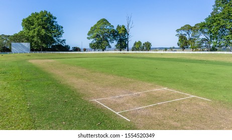 Scenic cricket grounds from white boundary fence of grass field and grass pitch morning  summer blue day countryside landscape.