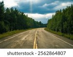 Scenic curved road cutting through lush green forests under a dramatic cloudy sky, depicting the natural beauty and wilderness of Canada.