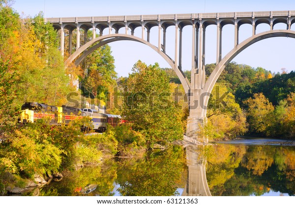 A\
scenic excursion train passes under a high arch\
bridge