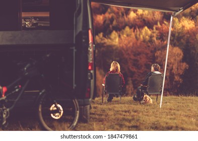 Scenic Fall Foliage RV Camper Camping. Caucasian Couple Seating Next To Their Motorhome And Enjoying The Scenery. Campsite Pitch.