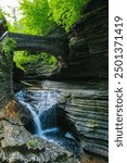 A scenic forest waterfall with multiple cascades, a stone bridge, and lush greenery creates a serene, Watkins Glen State Park, Pennsylvania