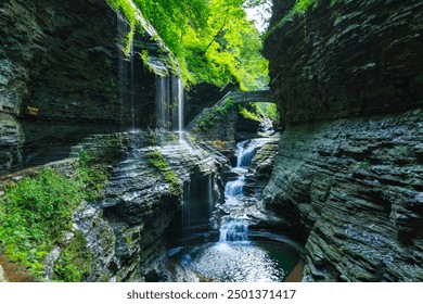 A scenic forest waterfall with multiple cascades, a stone bridge, and lush greenery creates a serene, Watkins Glen State Park, Pennsylvania - Powered by Shutterstock