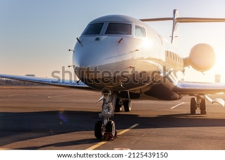 Scenic front view modern luxury expensive private jet plane parked airport taxiway hangar warm colorful dramatic evening warm sunset sun light sky background. Executive aicraft vip travel concept Imagine de stoc © 